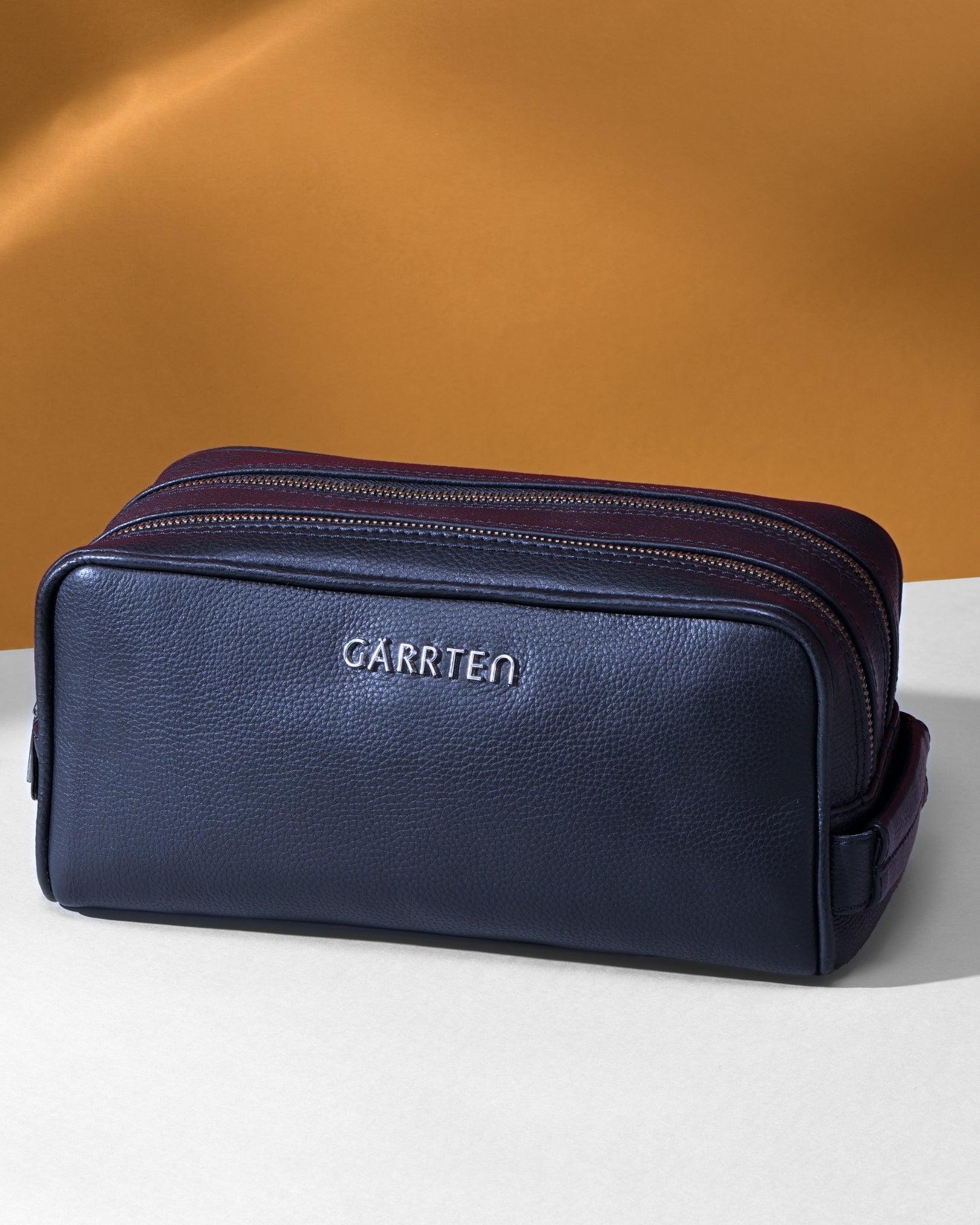 Midnight blue toiletry bag with 'Garrten' branding on a white surface with a brown background