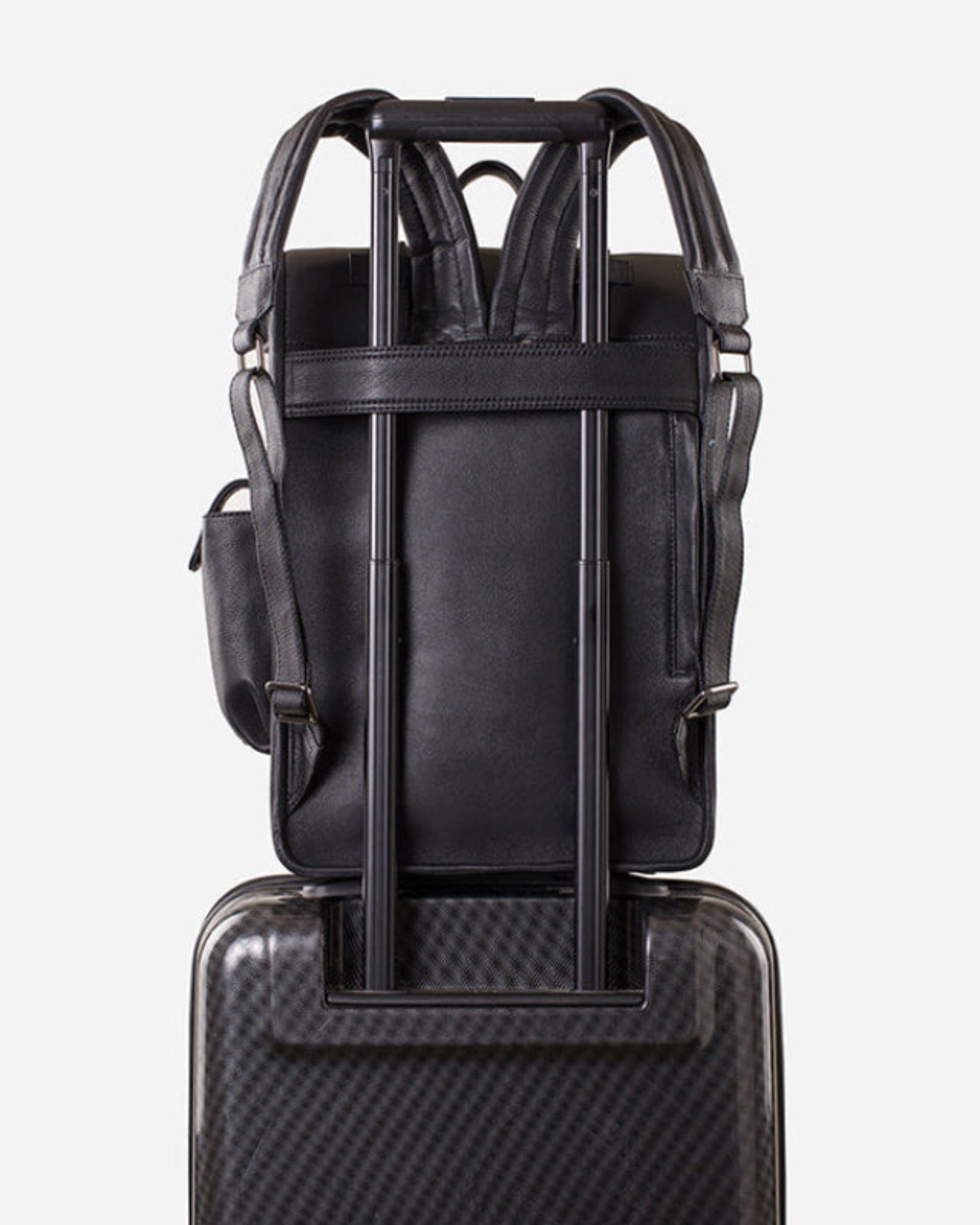 GARRTEN 751 rolltop full-grain leather backpack in midnight blue — back view with trolley sleeve pass-through on wheeled luggage demonstrating airline carry-on compatibility, white background