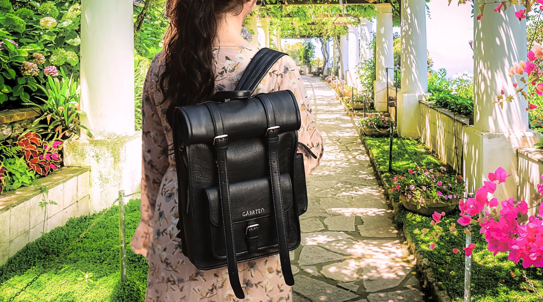 girl holding rolltop style leather backpack by garrten in carbon black. girl is on path in a garden.