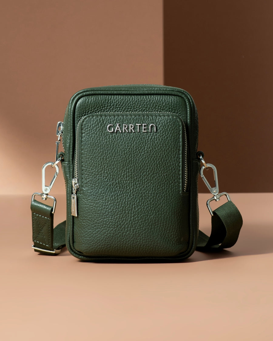 GARRTEN 508 mini Italian leather crossbody bag in forest green — hero mood shot with polished silver hardware on warm brown background